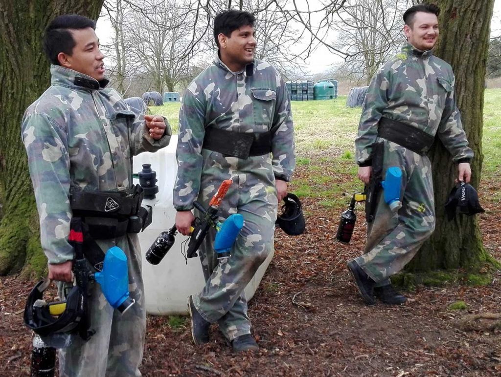 Three paintballers holding guns having a break whilst chatting after playing a game of capture the flag.