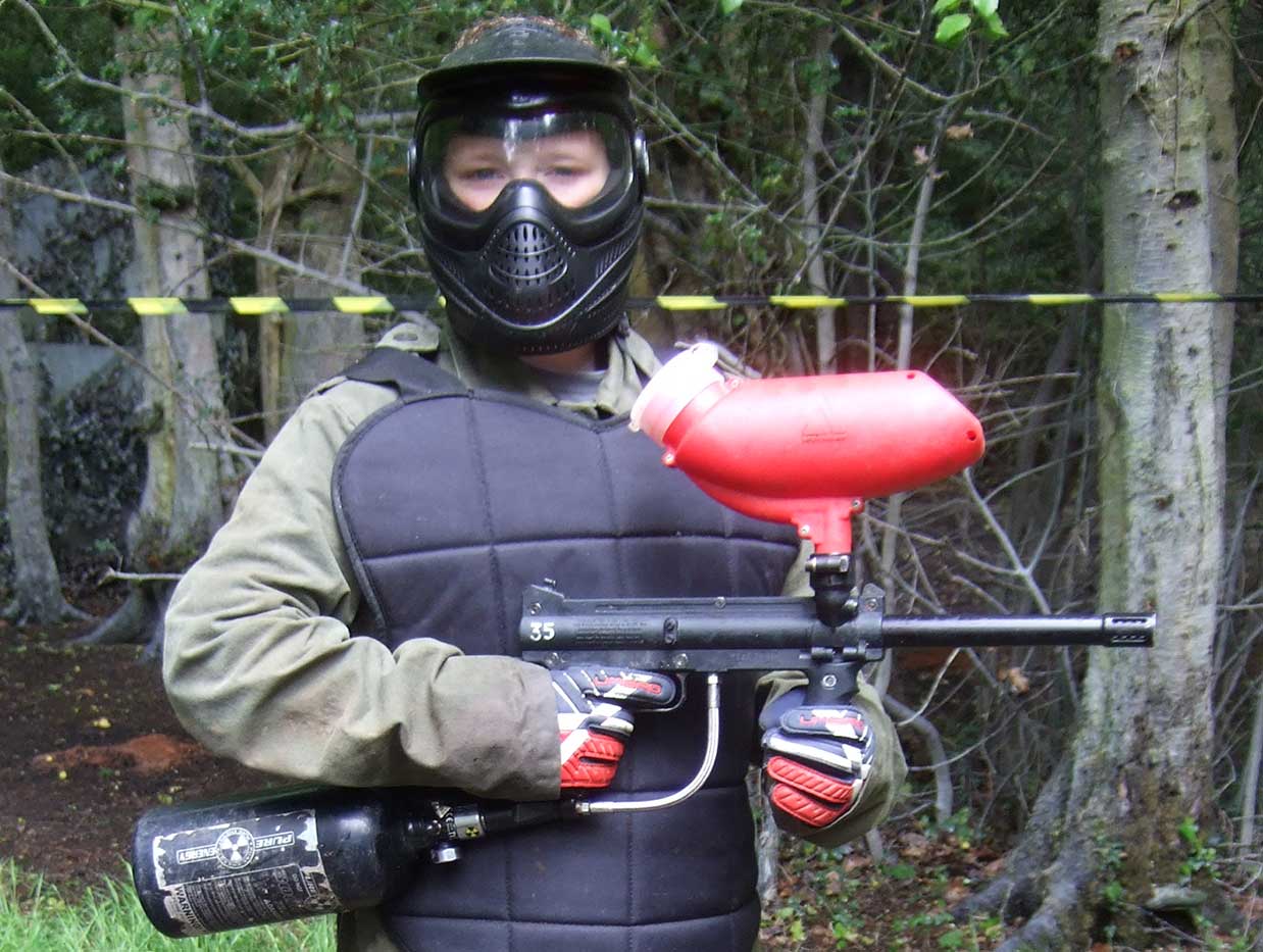 Youth holding a Tippmann 98 paintball gun whilst wearing body protection before a game.