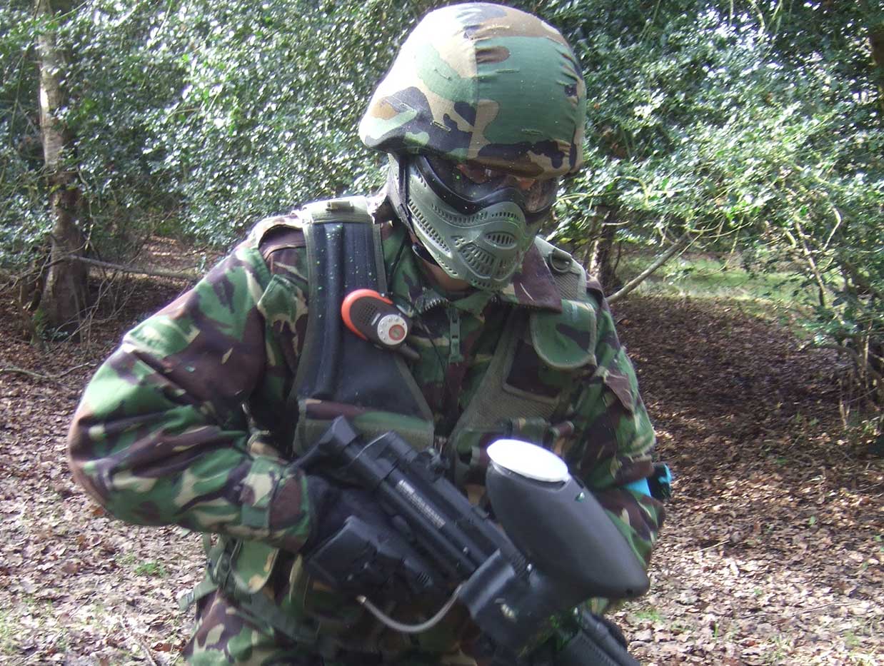 Camouflage paintball player wearing helmet and mask storms the opposition base with his gun.