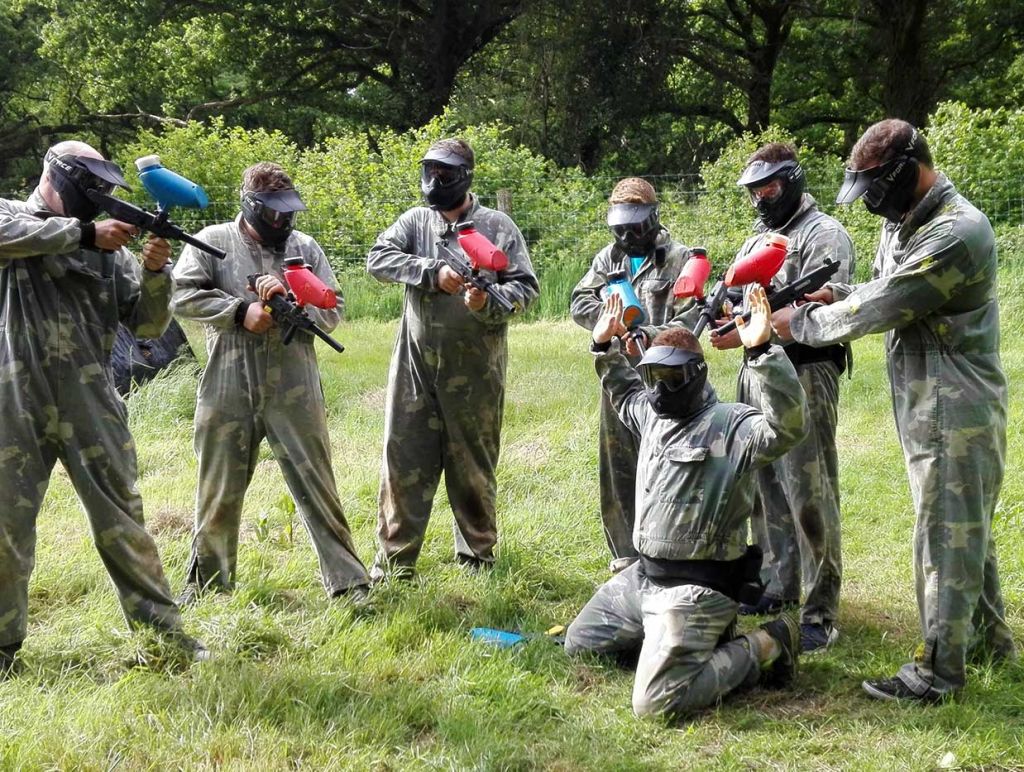 Stag party surrounds the groom aiming their paintball guns at his head as he surrenders.