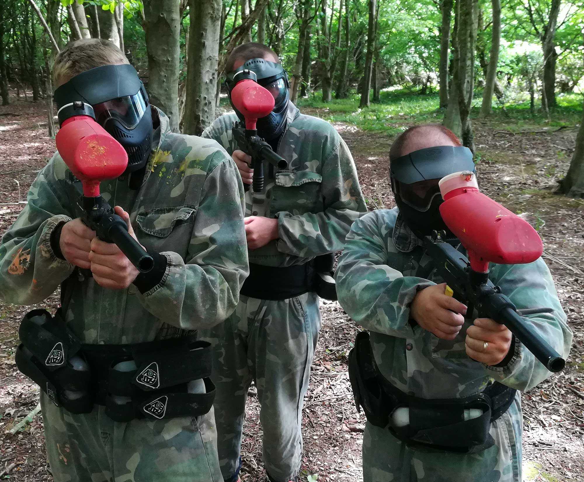 3 members of stag party on the red team playing paintball in the woods
