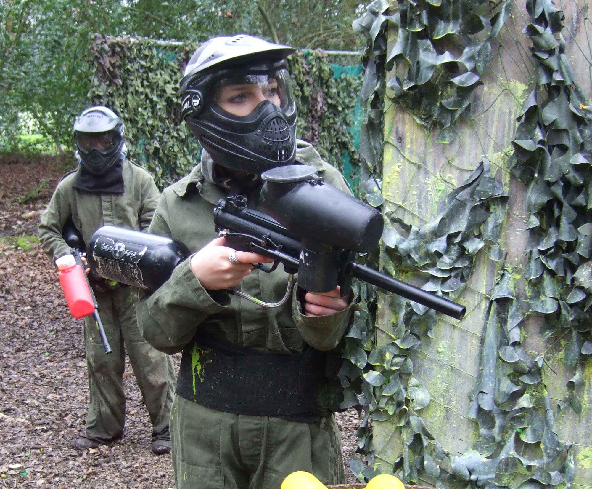 A member of a hen paintball party looks around cover holding a Tippmann A5