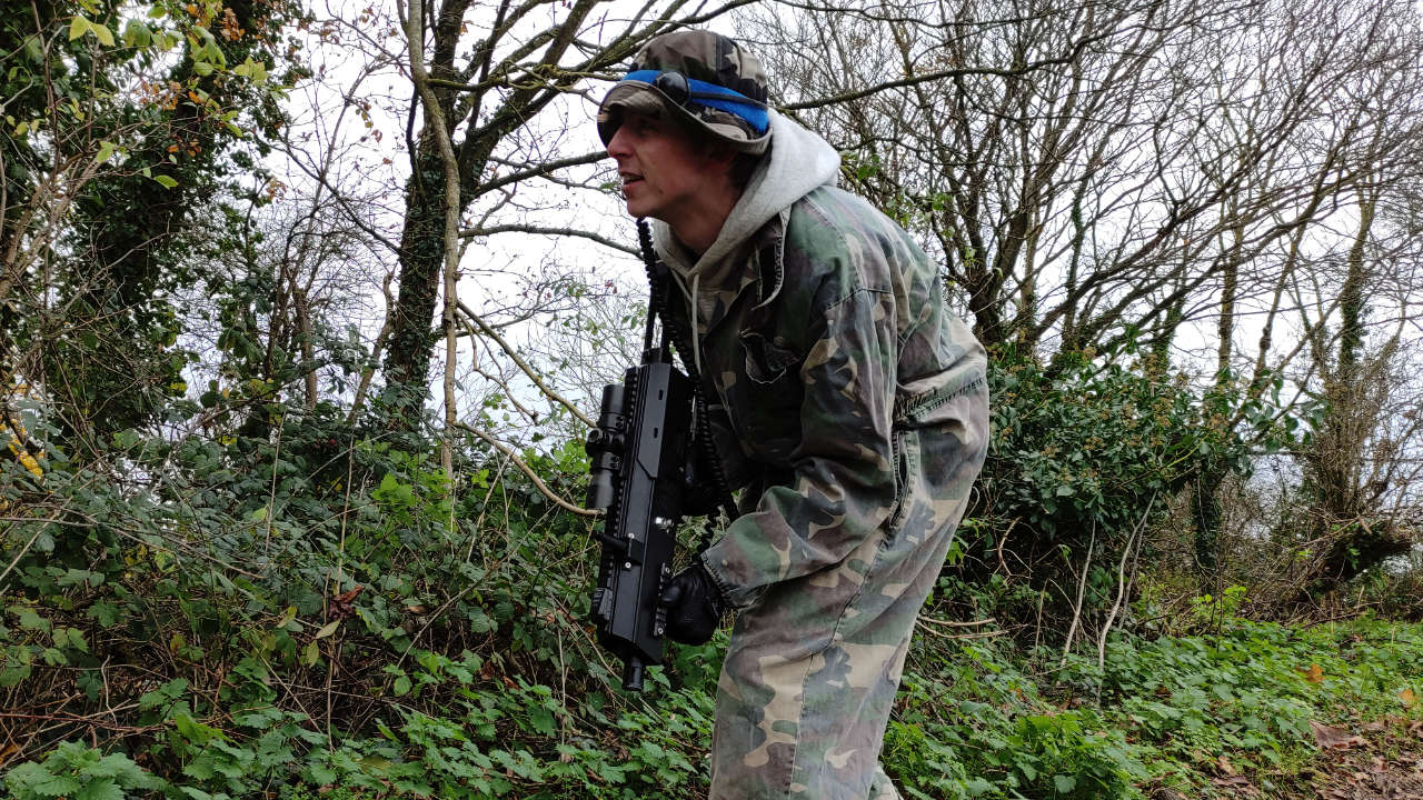 Blue team laser tag player advancing carefully down a hedge row.